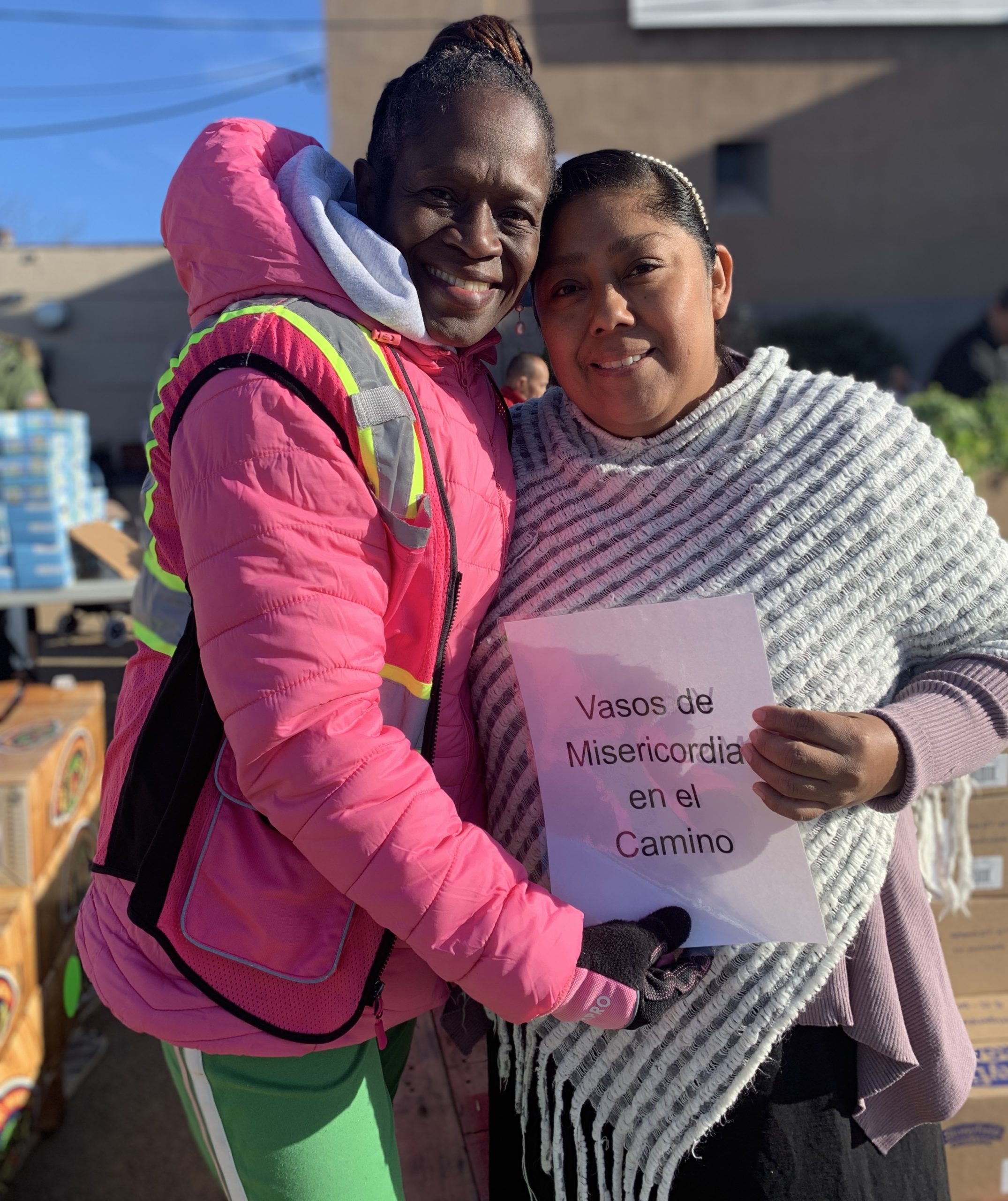 2 happy women holding a sign reading "Vasos de Misericodia en el Camino"