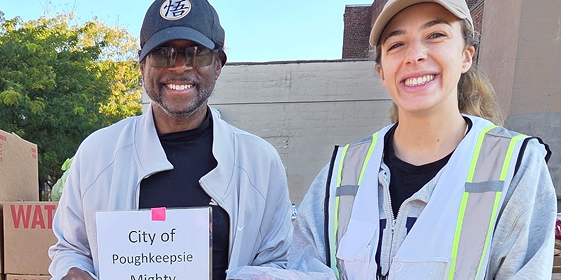 2 smiling people, holding a sign that says, "City of Poughkeepsie Mighty"